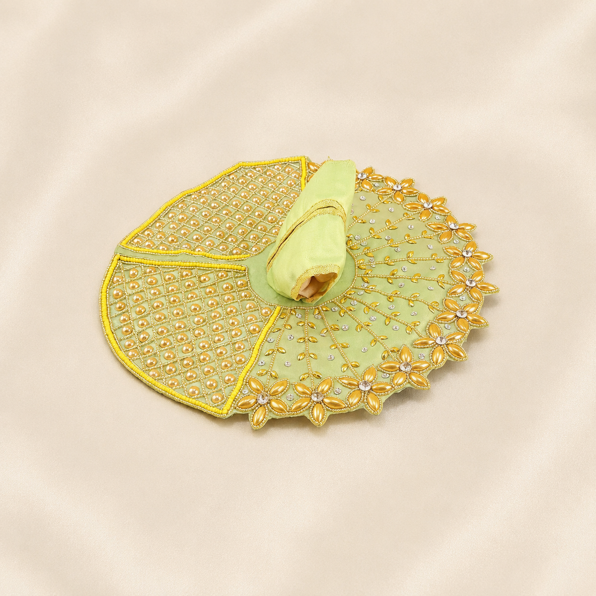 A light green embroidered accessory with gold floral embroidery and rhinestone embellishments, displayed on a beige satin fabric background.