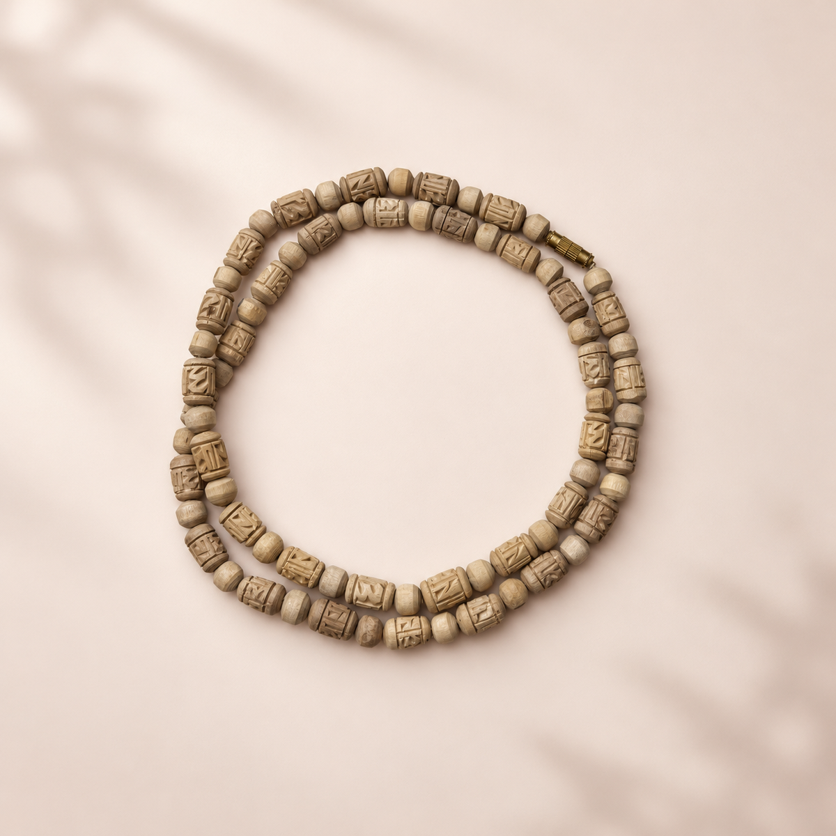 Tulsi wood Kanthi Mala with intricately carved cylindrical beads, round wooden spacers and gold-tone clasp on a pastel beige background.
