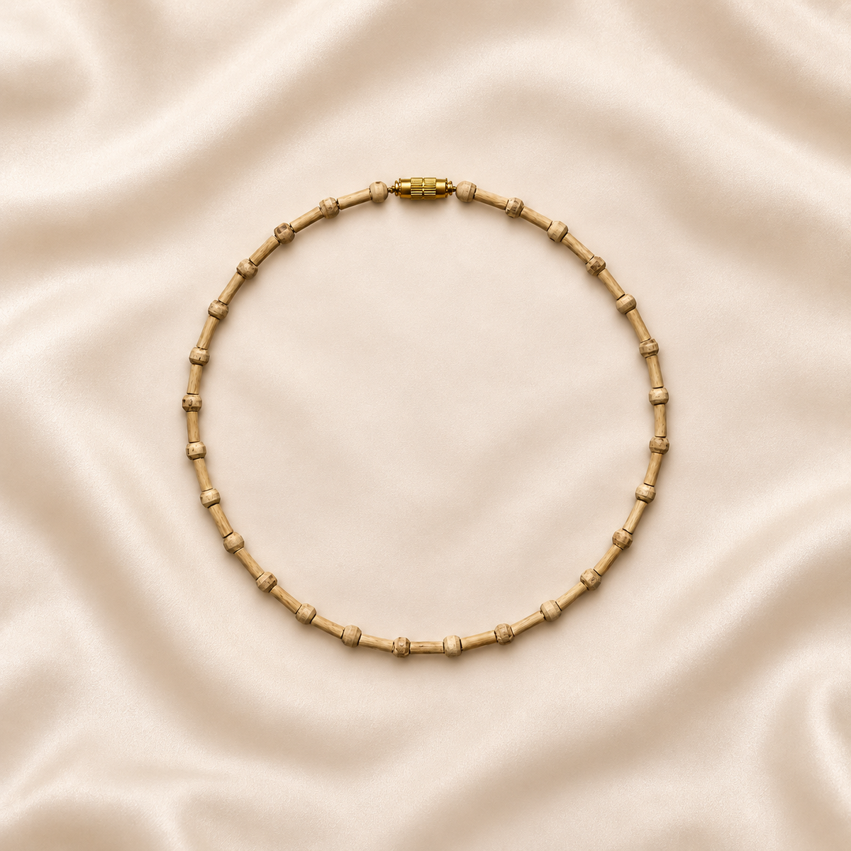 Natural Tulsi wood Kanthi Mala necklace with cylindrical wooden beads, round spacer beads and gold-tone clasp, arranged in a circular shape on cream silk fabric.