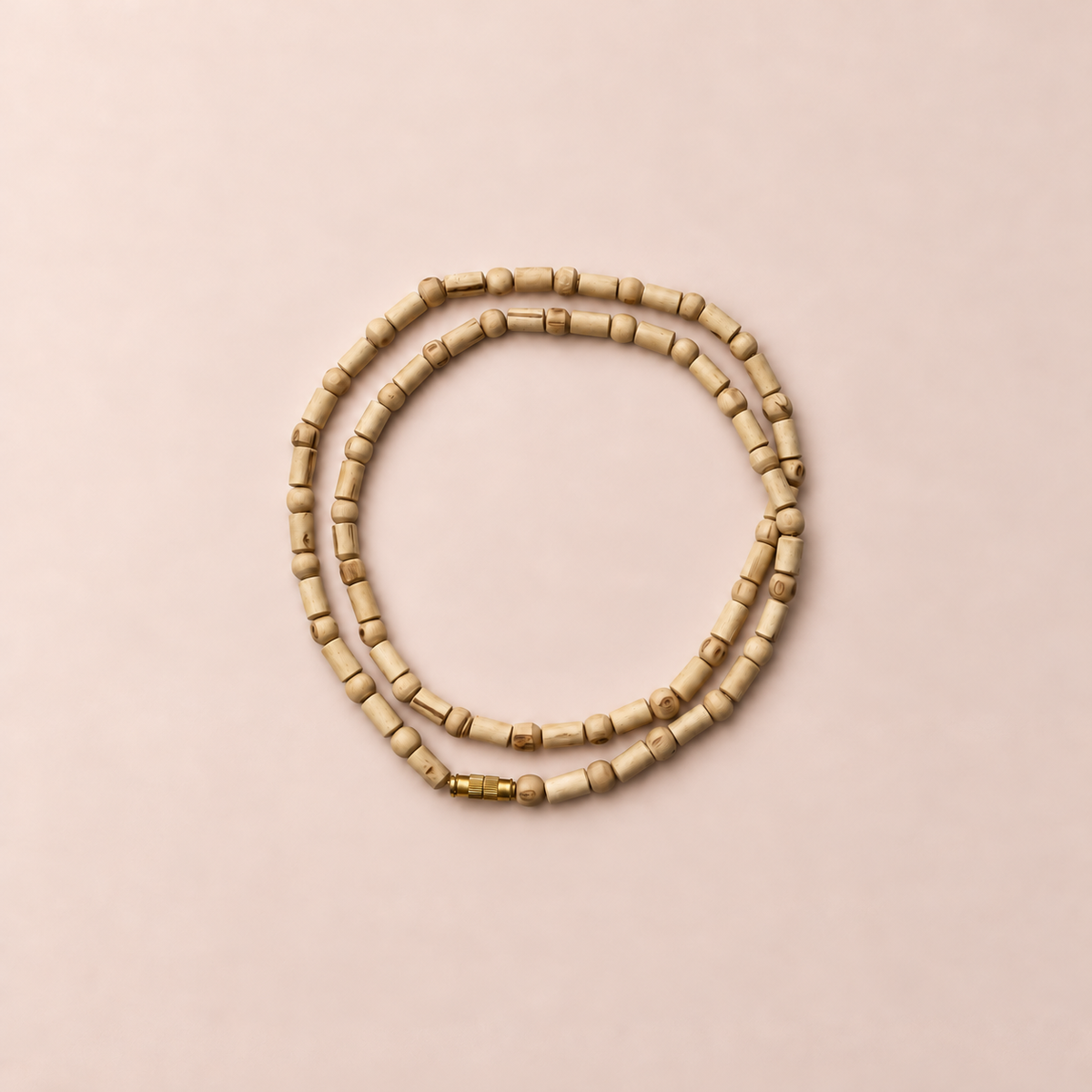 Natural Tulsi wood Kanthi Mala with cylindrical and round handcrafted wooden beads, gold-tone screw clasp, arranged in a double circular loop on a pastel beige background.