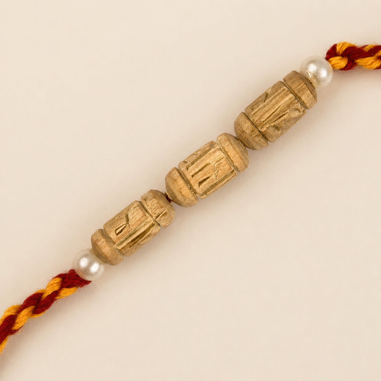 carved original Tulsi wood beads flanked by white pearls on a red and yellow braided Rakhi thread.