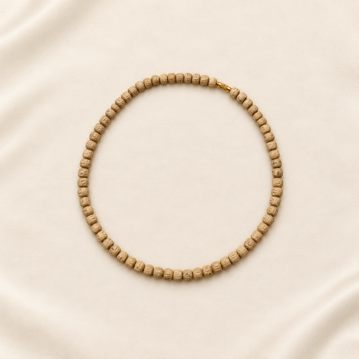 Original Tulsi wood Kanthi Mala necklace with carved wooden beads and gold-tone clasp, arranged in a circular shape on an ivory fabric background.