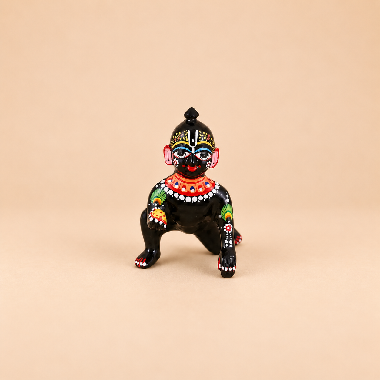 A small black laddu gopal decorated with colorful hand-painted traditional patterns, set against a solid beige background.
