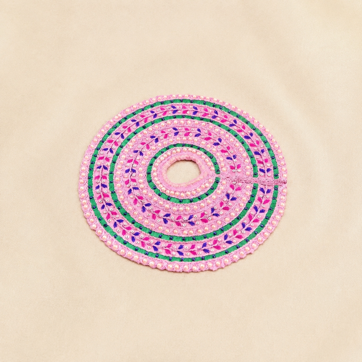 Pink circular Laddu Gopal dress with pearl borders, green embroidered bands, purple leaf motifs and decorative stones