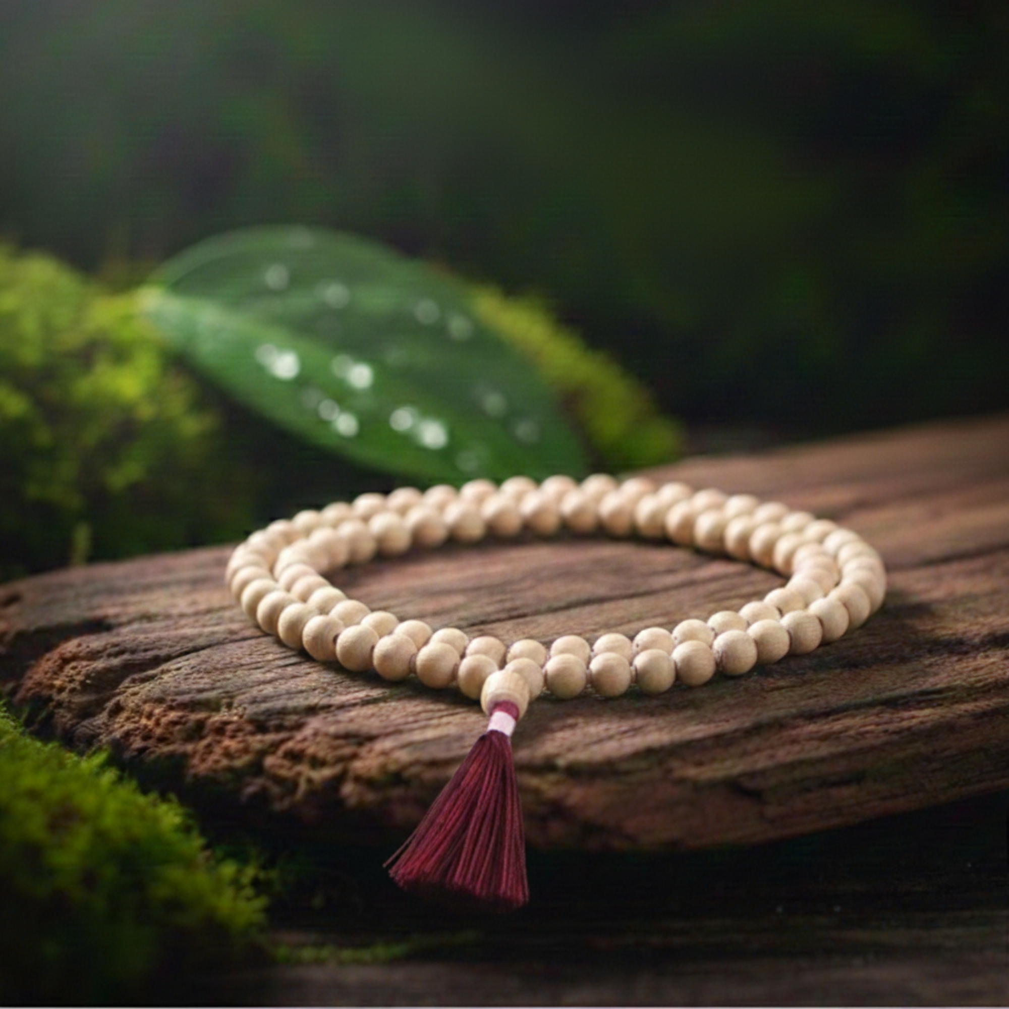 Premium certified 108 bead Tulsi japa mala with a red tassel resting on a mossy log