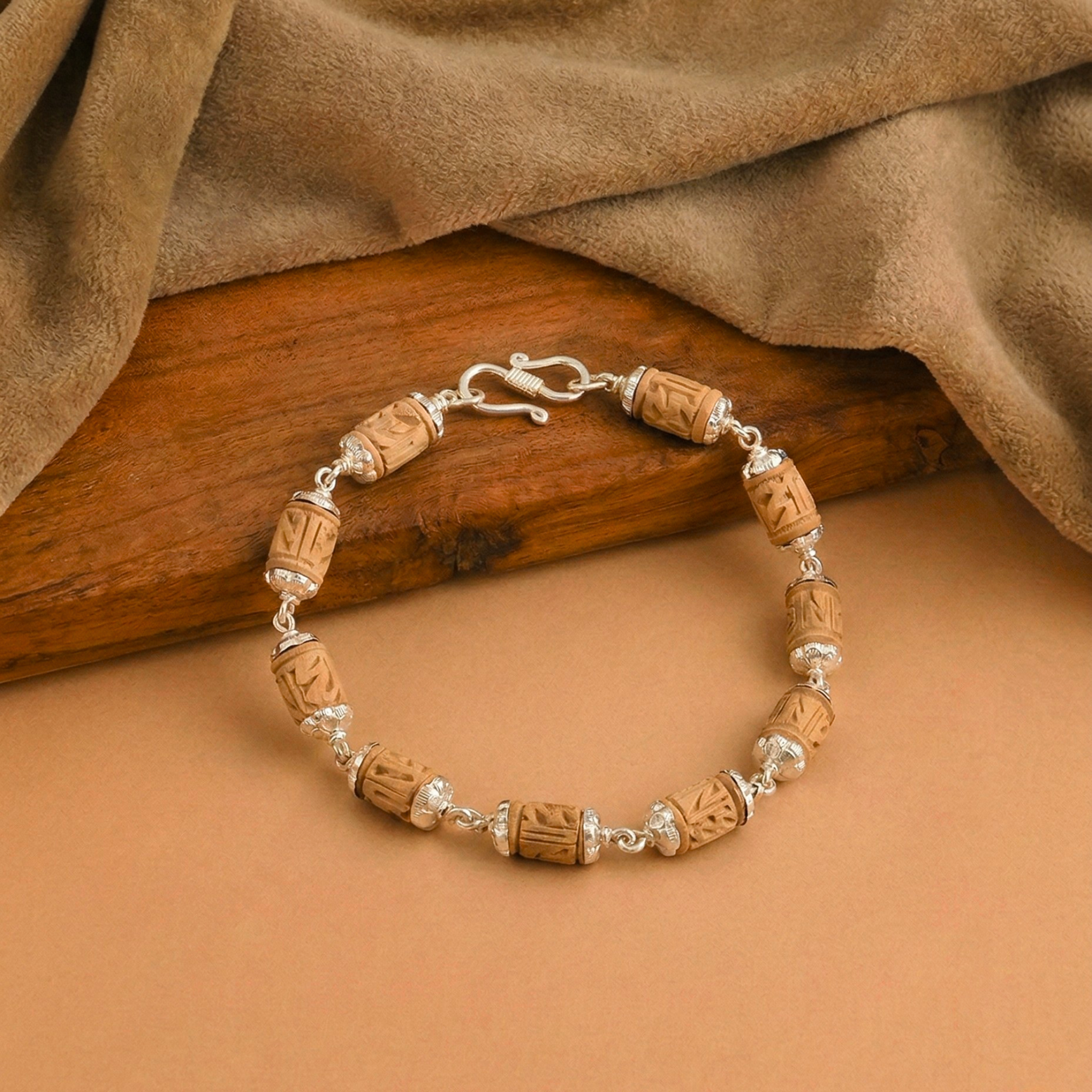 Pure silver bracelet featuring carved original Tulsi wood beads resting on a warm surface