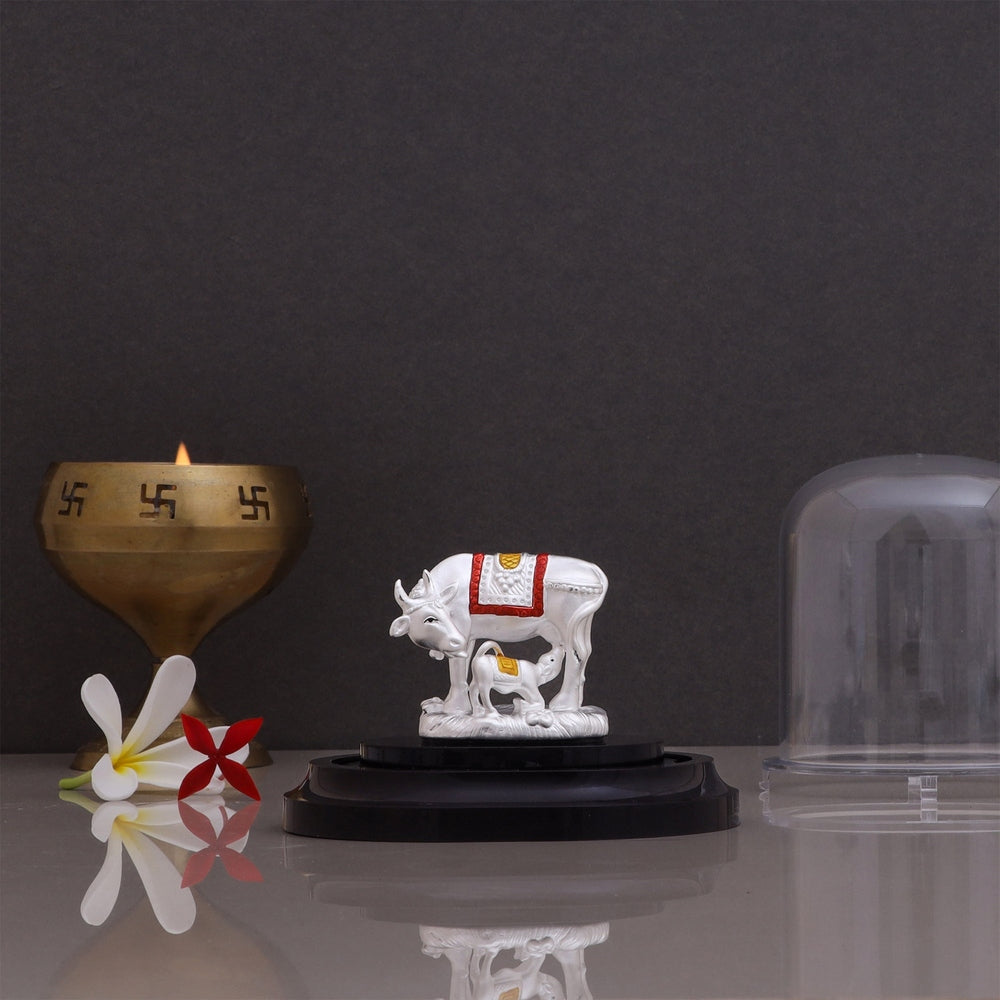 Pure silver Kamdhenu Cow with calf Vastu idol displayed on a stand with a brass diya