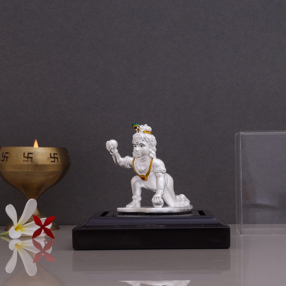 Pure silver Laddu Gopal idol with beautiful artistic work displayed on a black stand with a brass diya
