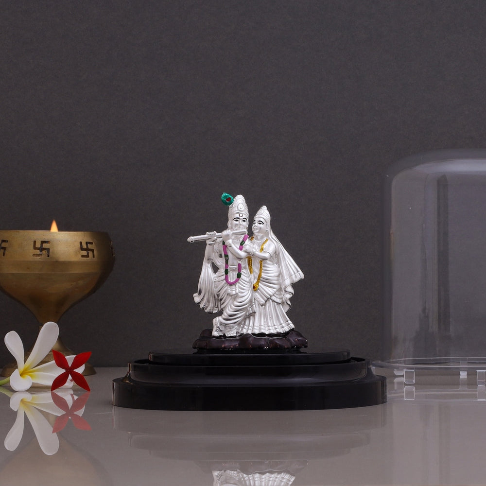 Pure silver Radha Krishna idol decorative showpiece displayed on a black stand with a brass diya