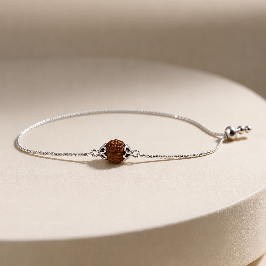 Pure silver capped single Rudraksha bead chain bracelet rakhi with silver charm on sand surface