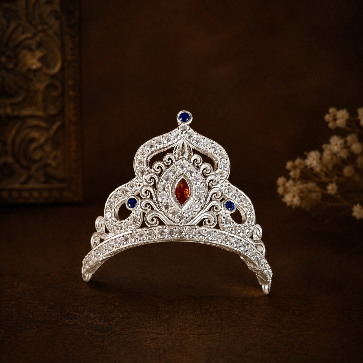Pure silver crown for Laddu Gopal with red and blue stones on dark wood background