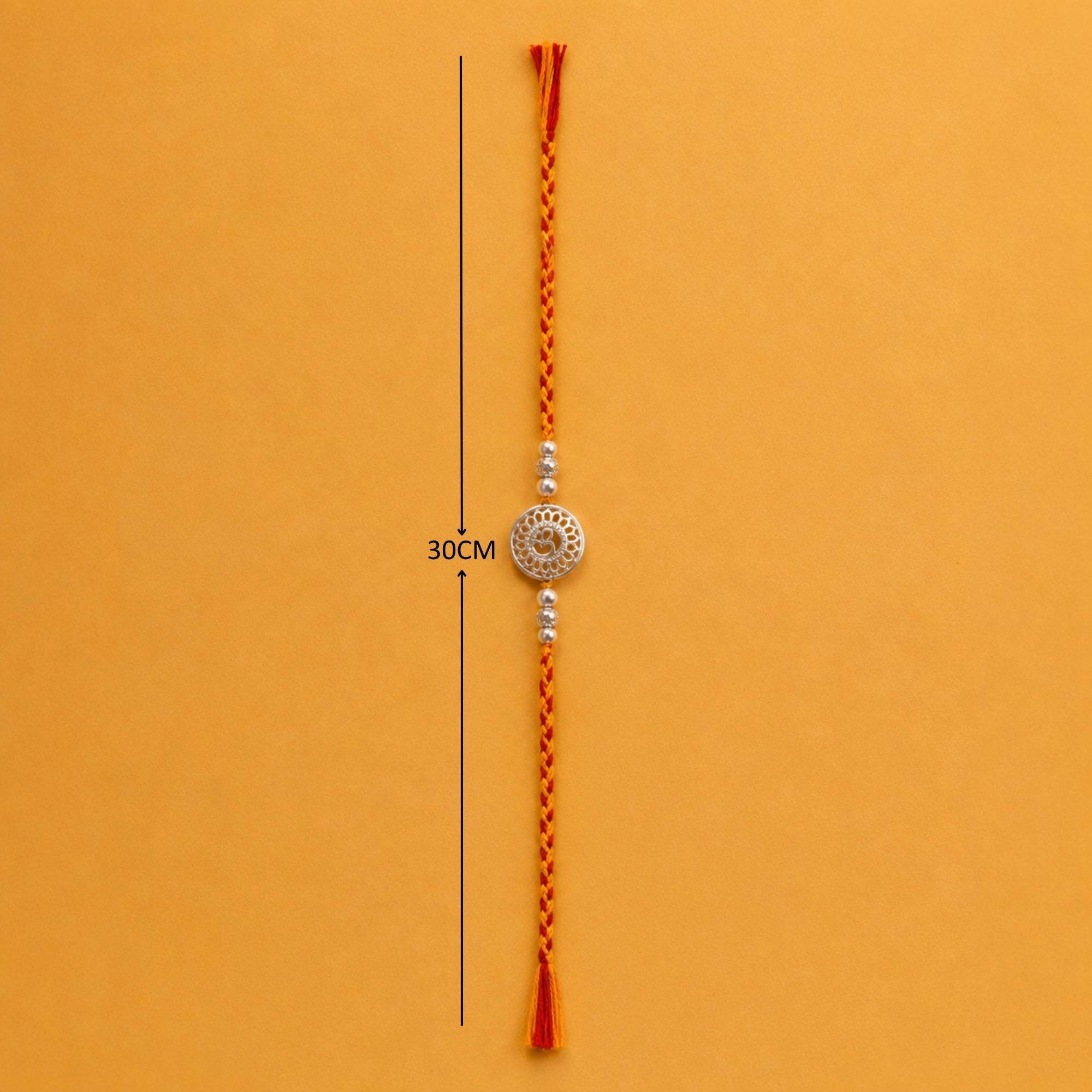 Full length view of pure silver Om rakhi on yellow orange thread layout