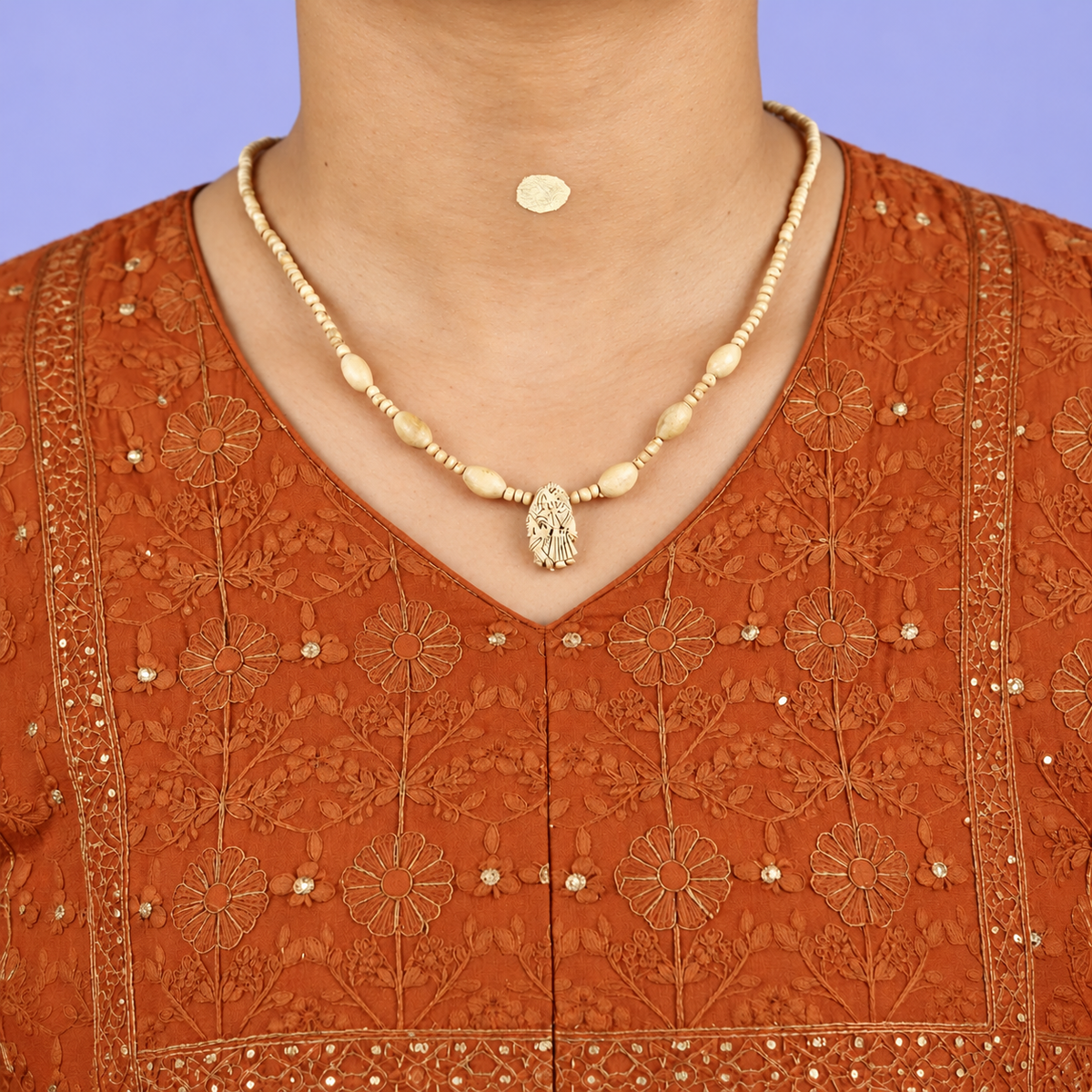 Tulsi mala with oval beads and a carved Radha Krishna pendant worn with an orange embroidered kurta.