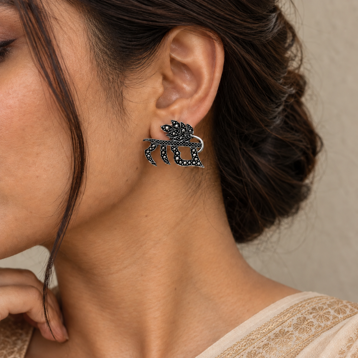 Close-up of a model wearing a black-and-silver-tone imitation earring featuring the name Radha with a decorative leaf design.