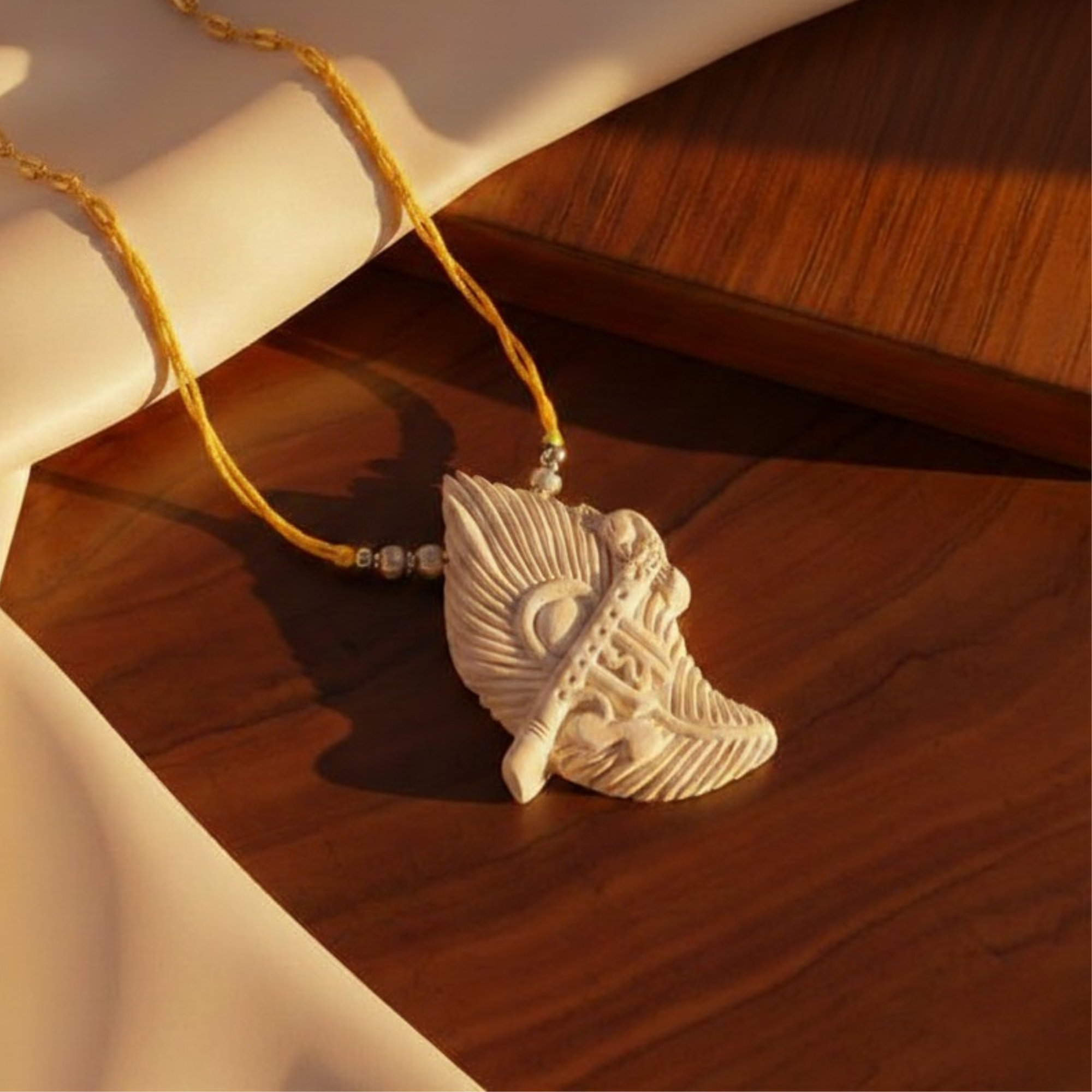 Person wearing a silver pendant featuring a peacock feather design and Radha name carved on Tulsi wood