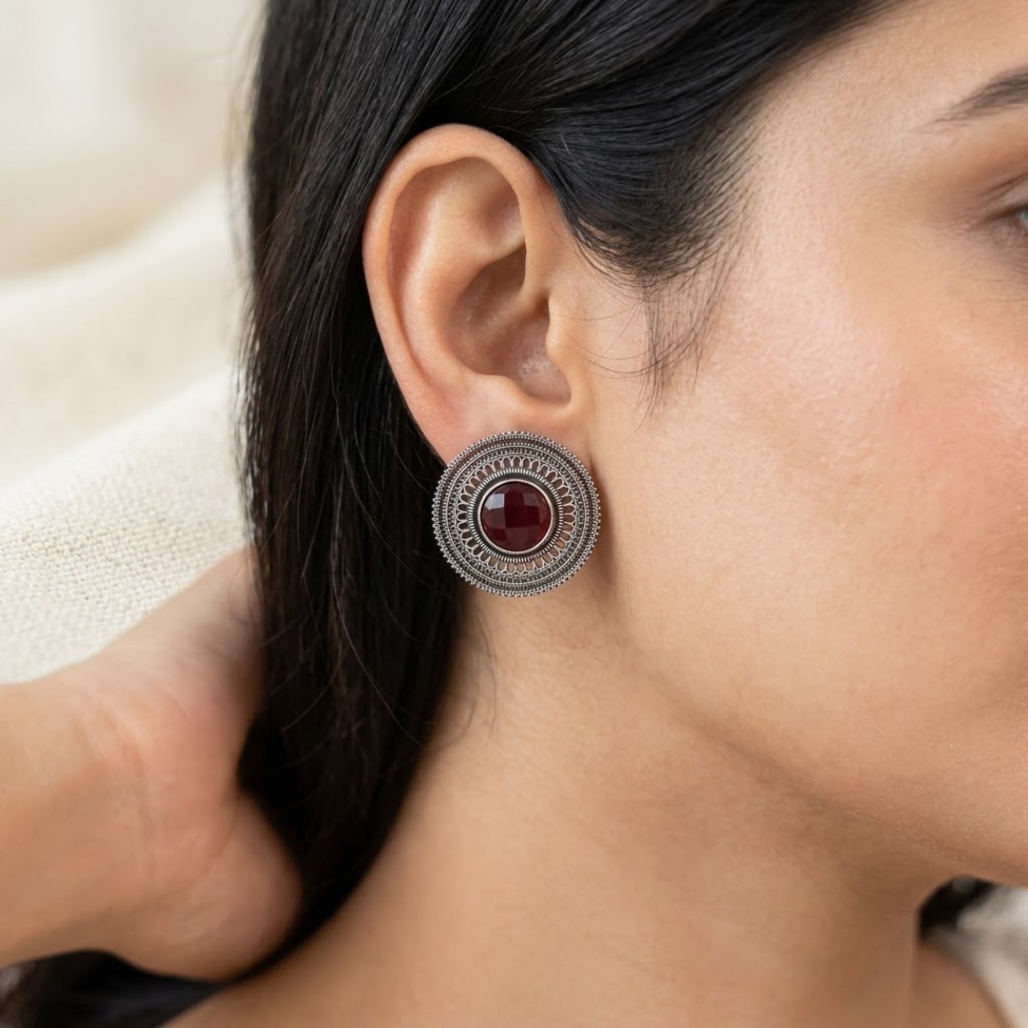 Red oxidized metal stud earring with round stone and detailed circular filigree design worn on ear