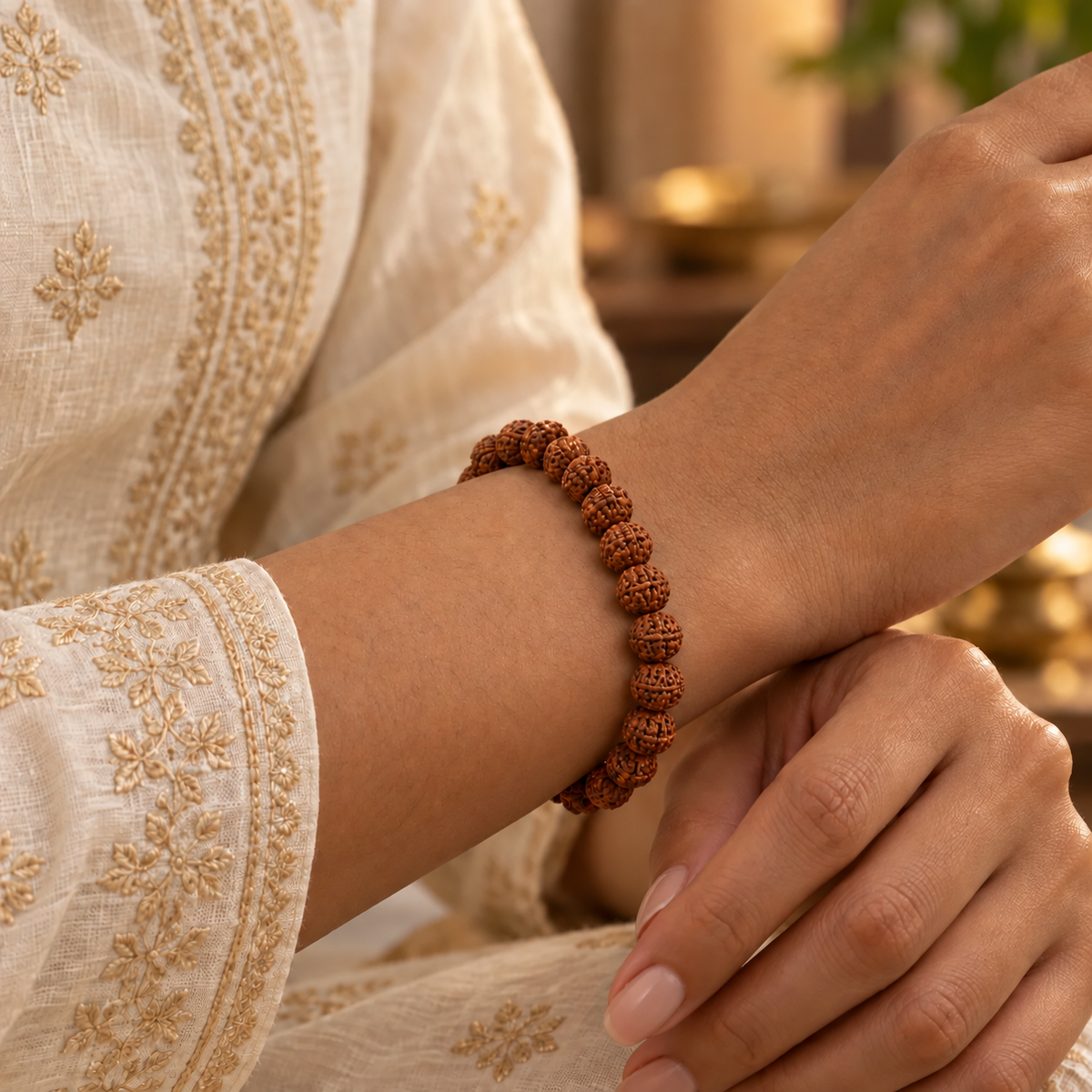 Brown Rudraksha bead bracelet worn on a woman's wrist with a cream embroidered kurta.