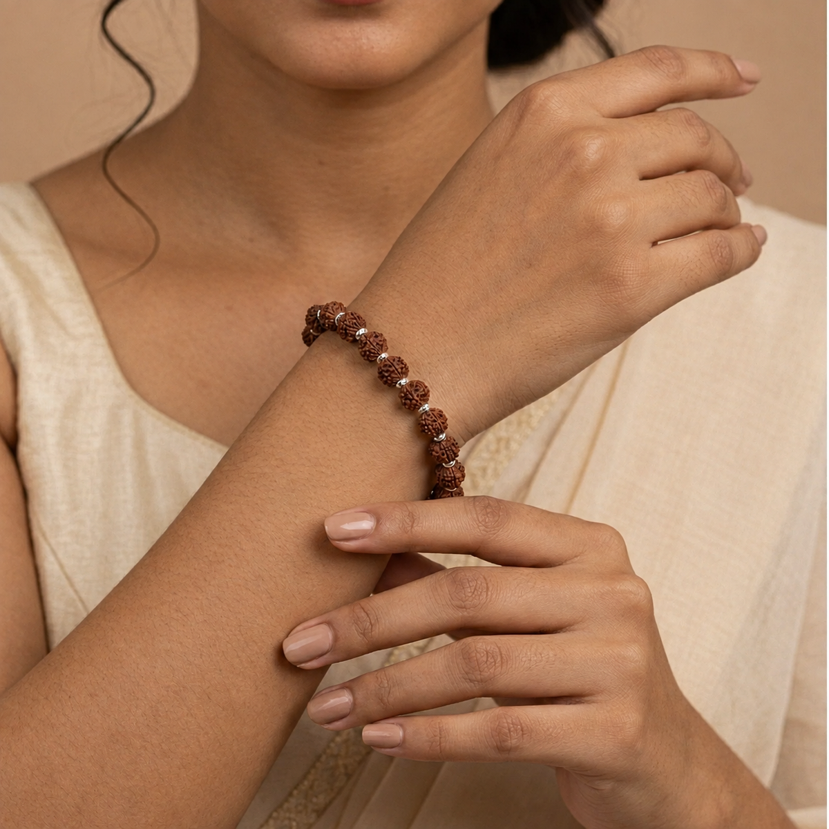 Rudraksha bracelet with brown beads and silver-toned spacers worn on a woman's wrist with a cream saree.