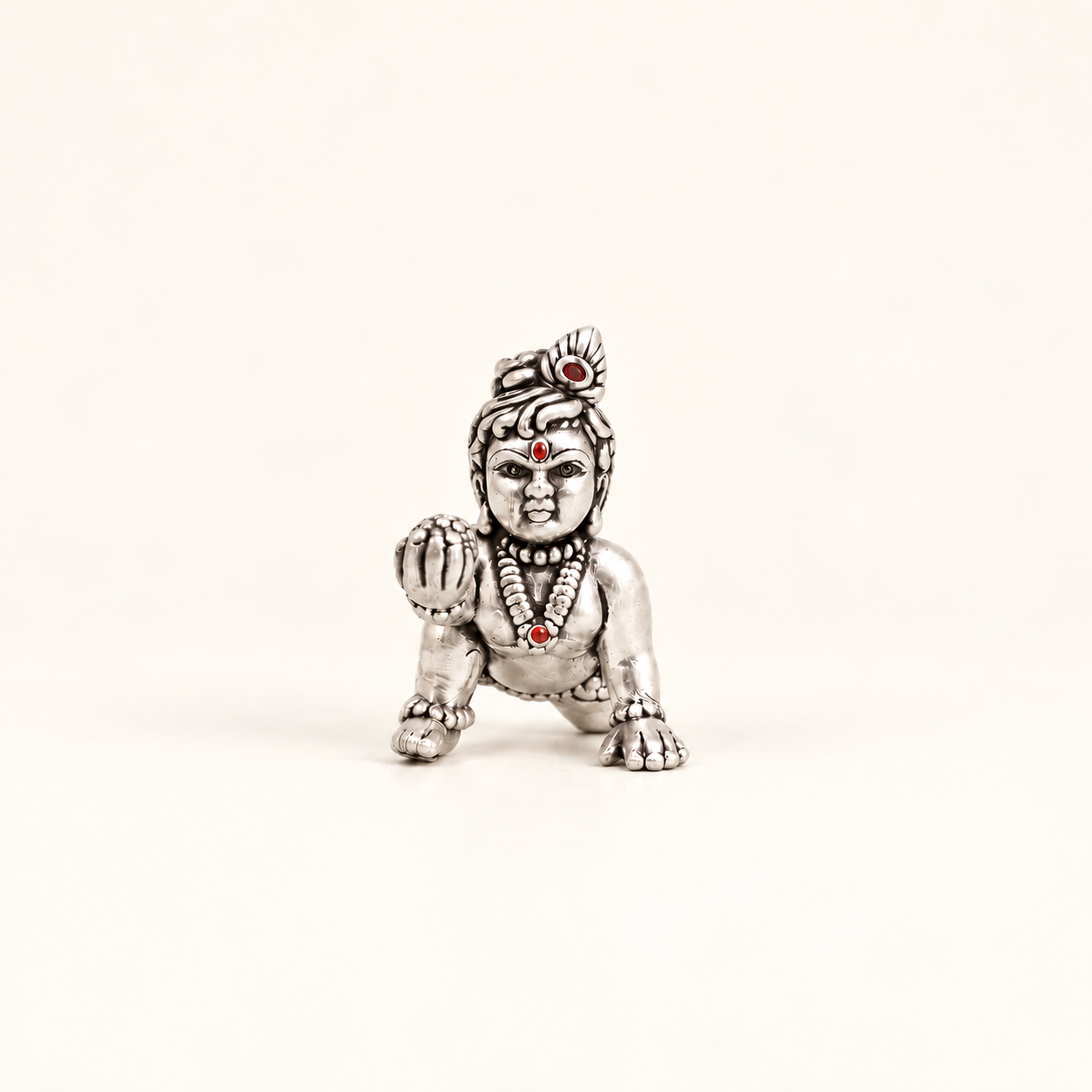 Front view of a silver crawling Laddu Gopal idol holding a sweet against an off-white background.