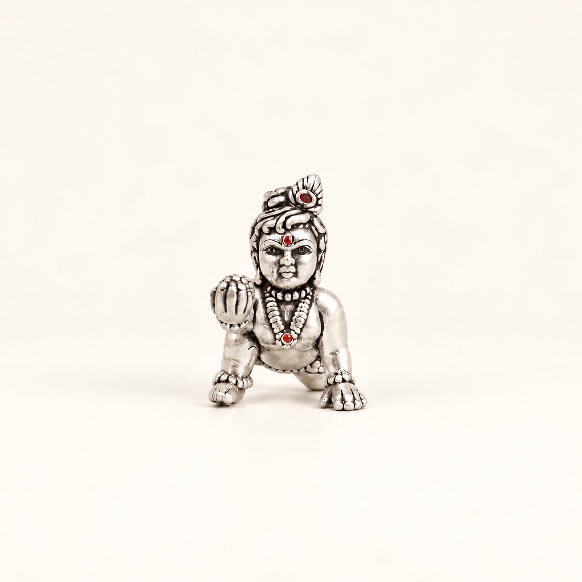 Front view of a silver crawling Laddu Gopal idol holding a sweet against an off-white background.