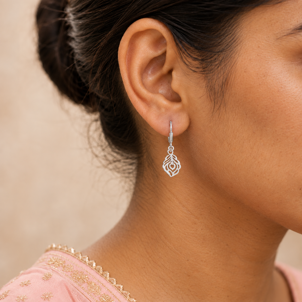 Silver peacock feather cutout earring with a clasp worn by a woman in pink.