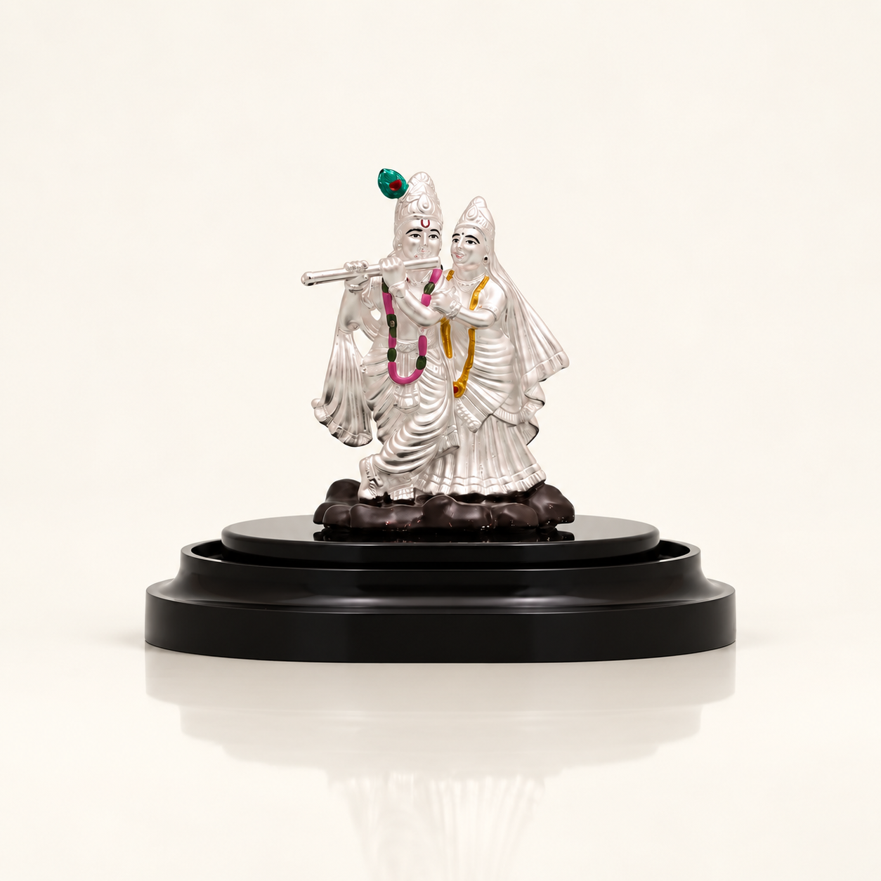Silver Radha Krishna idol with Krishna playing the flute on a dark display stand against an off-white background.