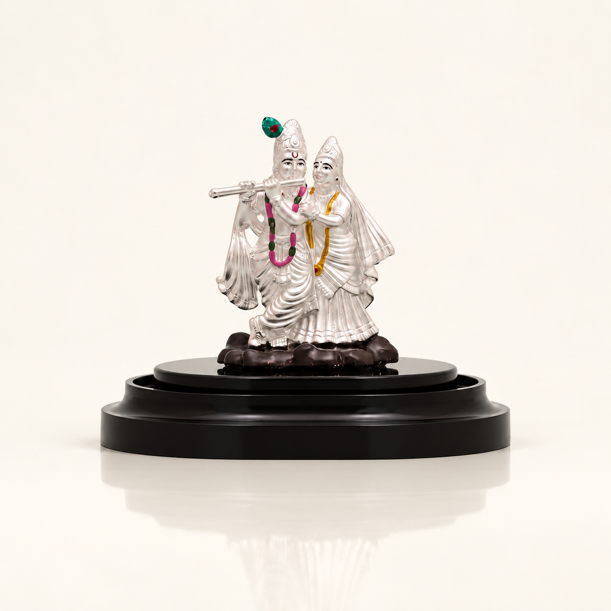 Silver Radha Krishna idol with Krishna playing the flute on a dark display stand against an off-white background.