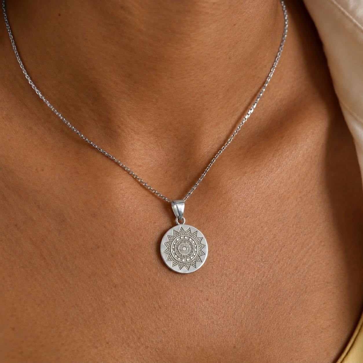 Close-up of a round silver pendant necklace with an engraved sun mandala design worn on a model.
