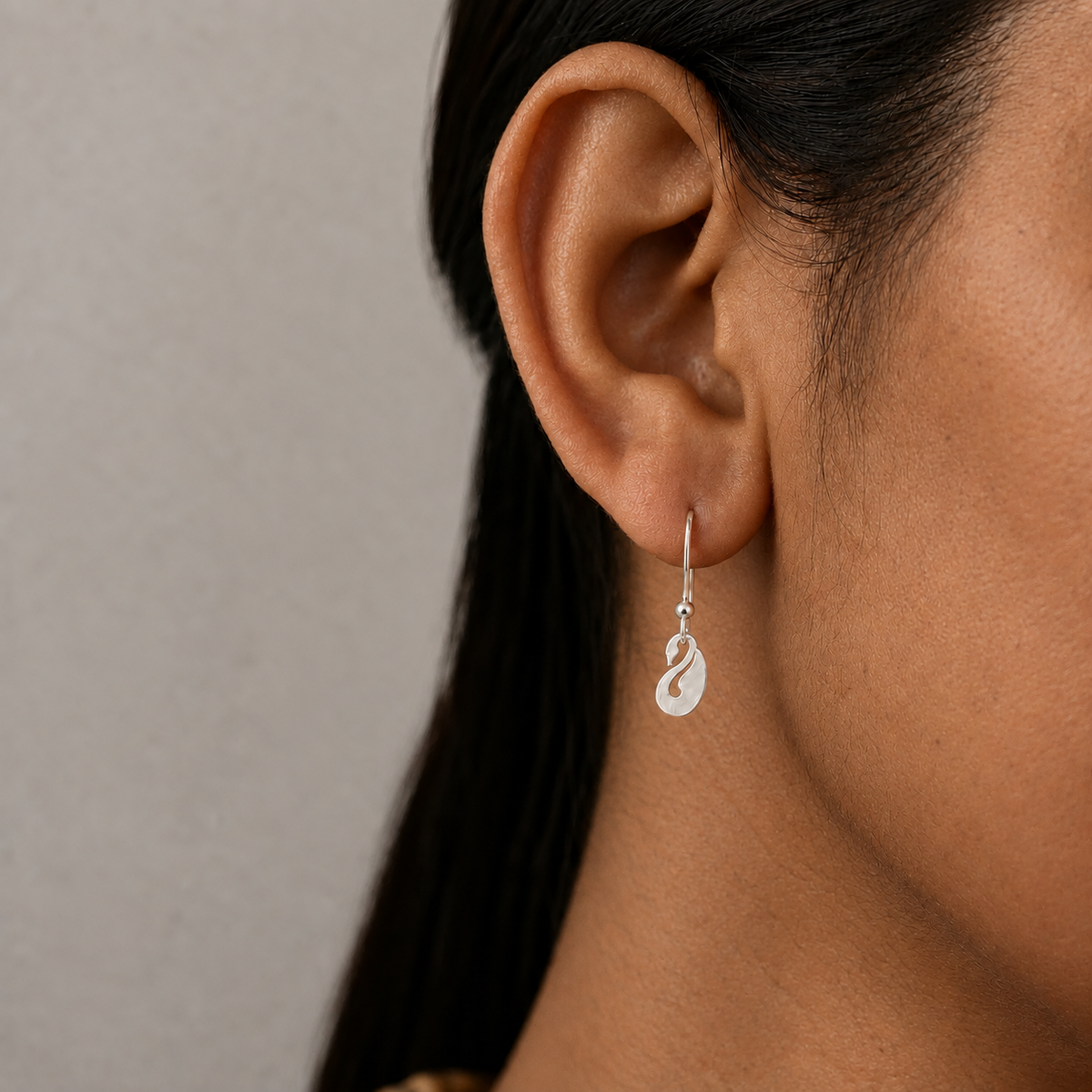 Silver swan-shaped drop earring worn on the ear.