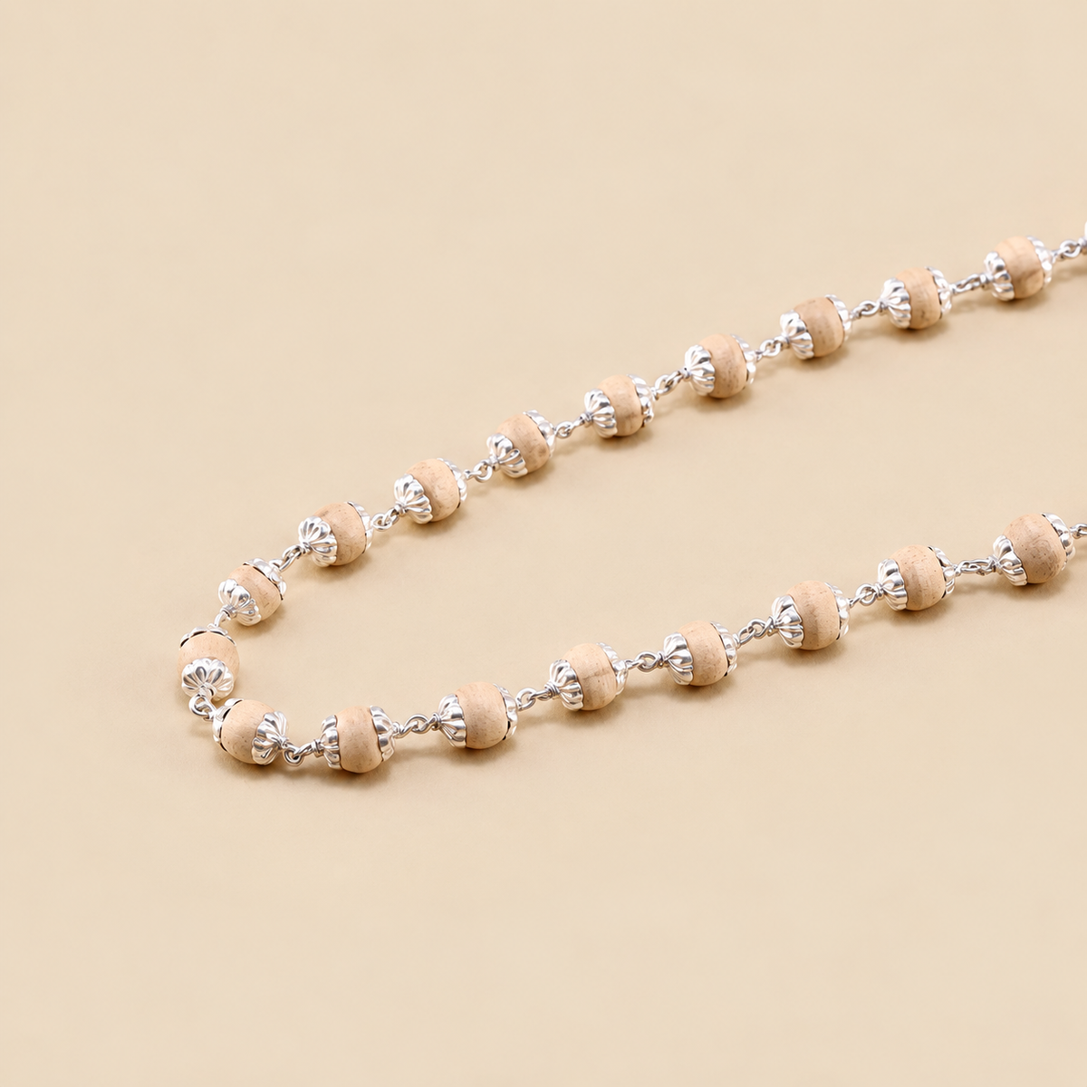 Close-up of silver Tulsi mala showing natural wooden bead texture, floral silver caps and connecting chain links on a beige background.