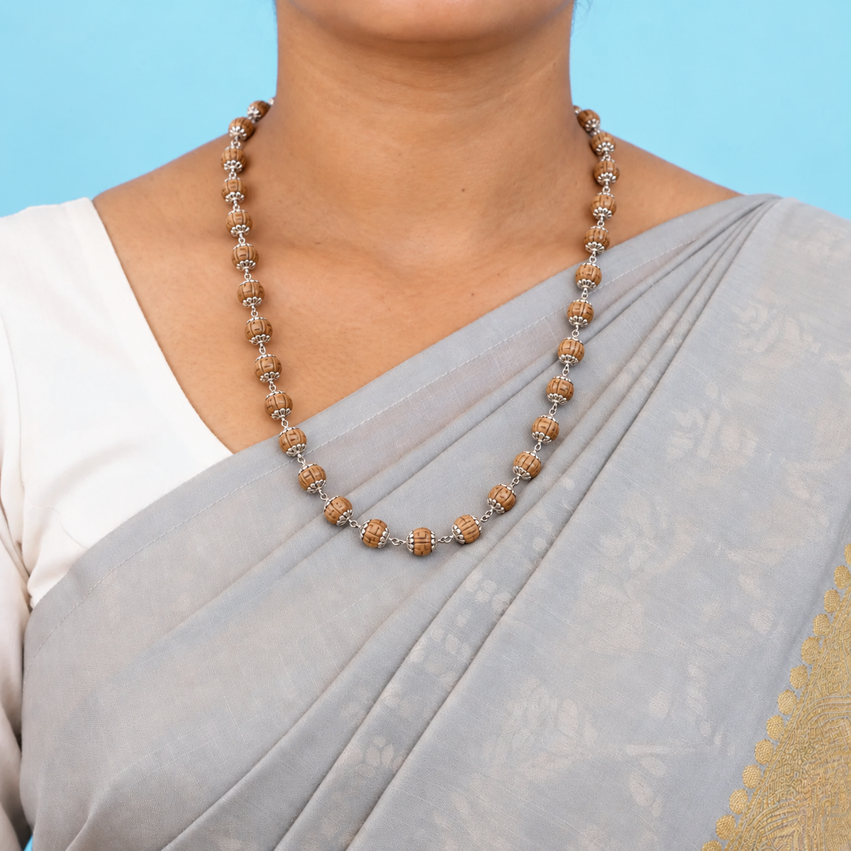 Woman wearing a silver Tulsi mala with natural wooden beads and detailed silver caps over a grey saree.