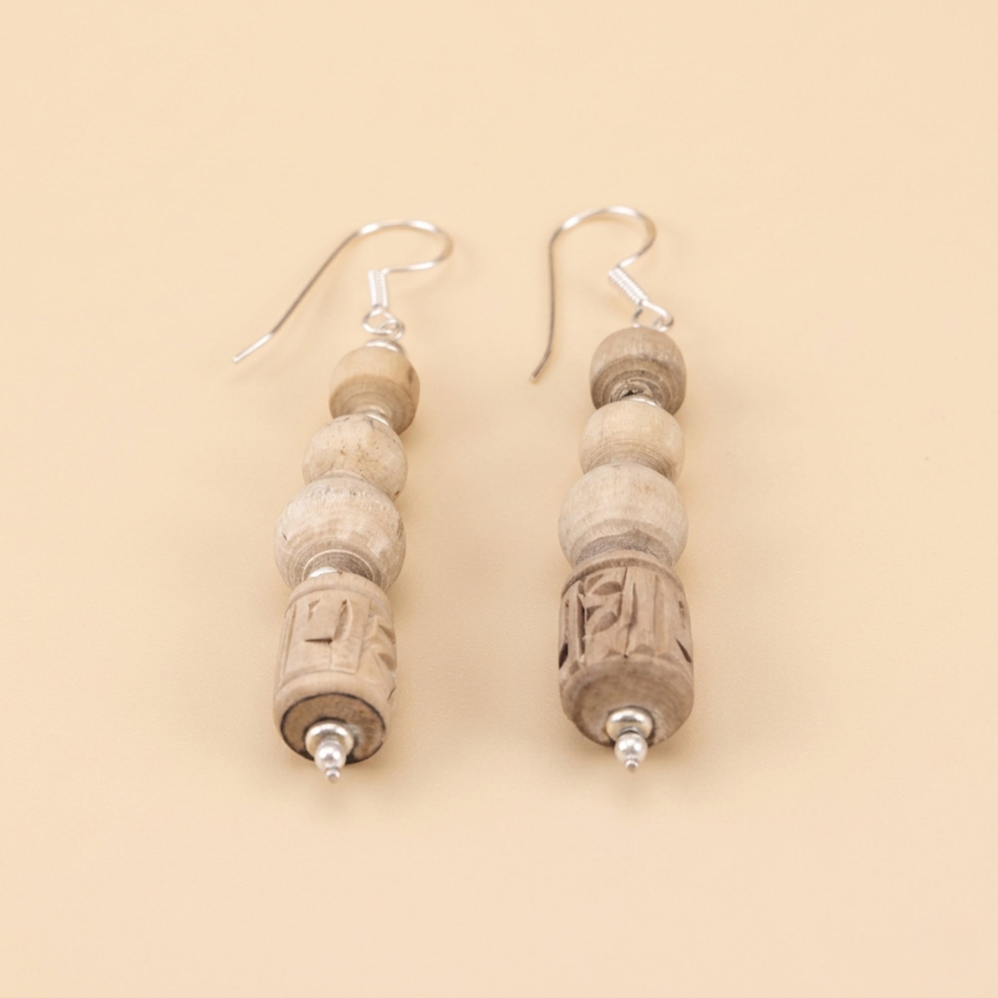 Close up flat lay of silver dangle earrings featuring carved Tulsi wood beads