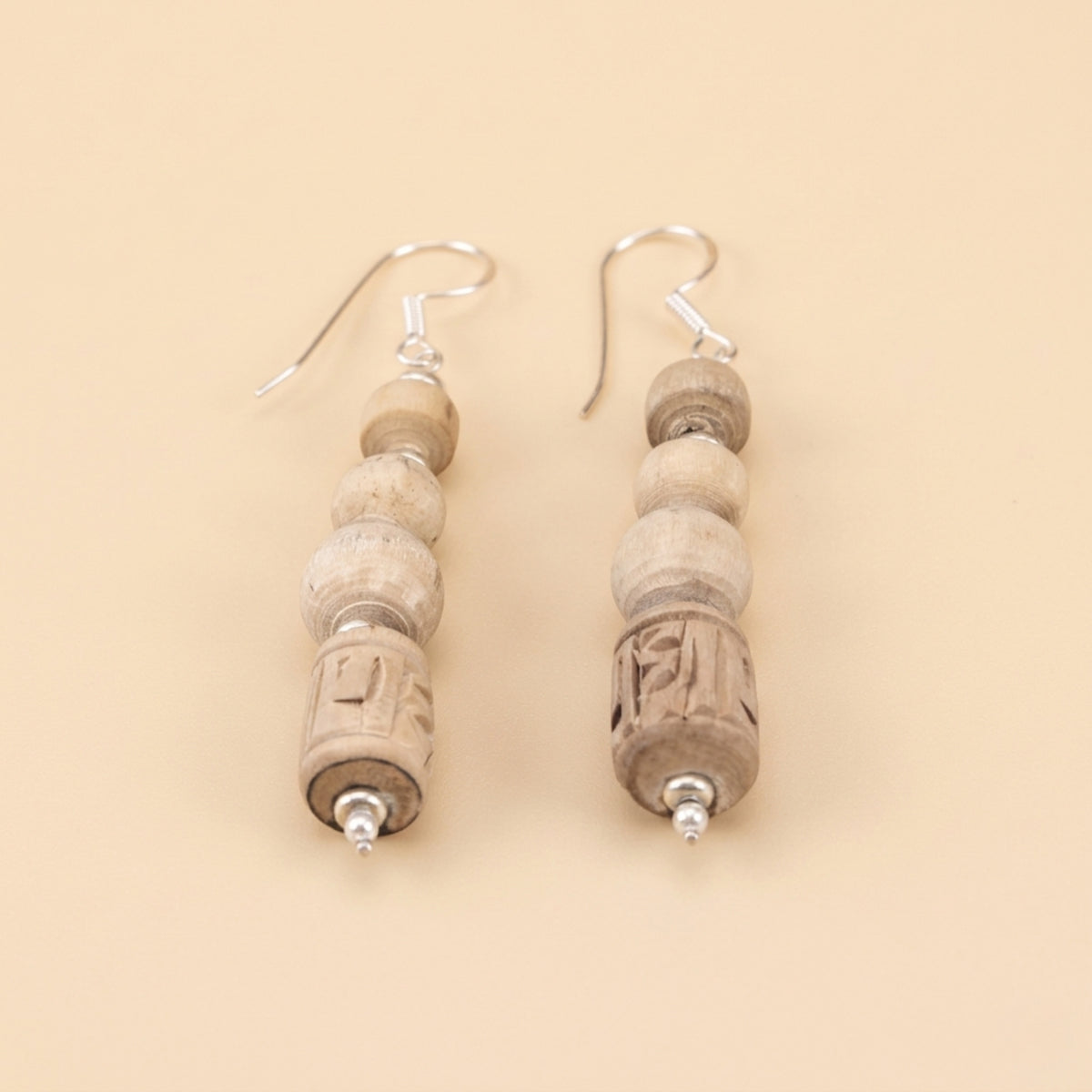 Close up flat lay of silver dangle earrings featuring carved Tulsi wood beads