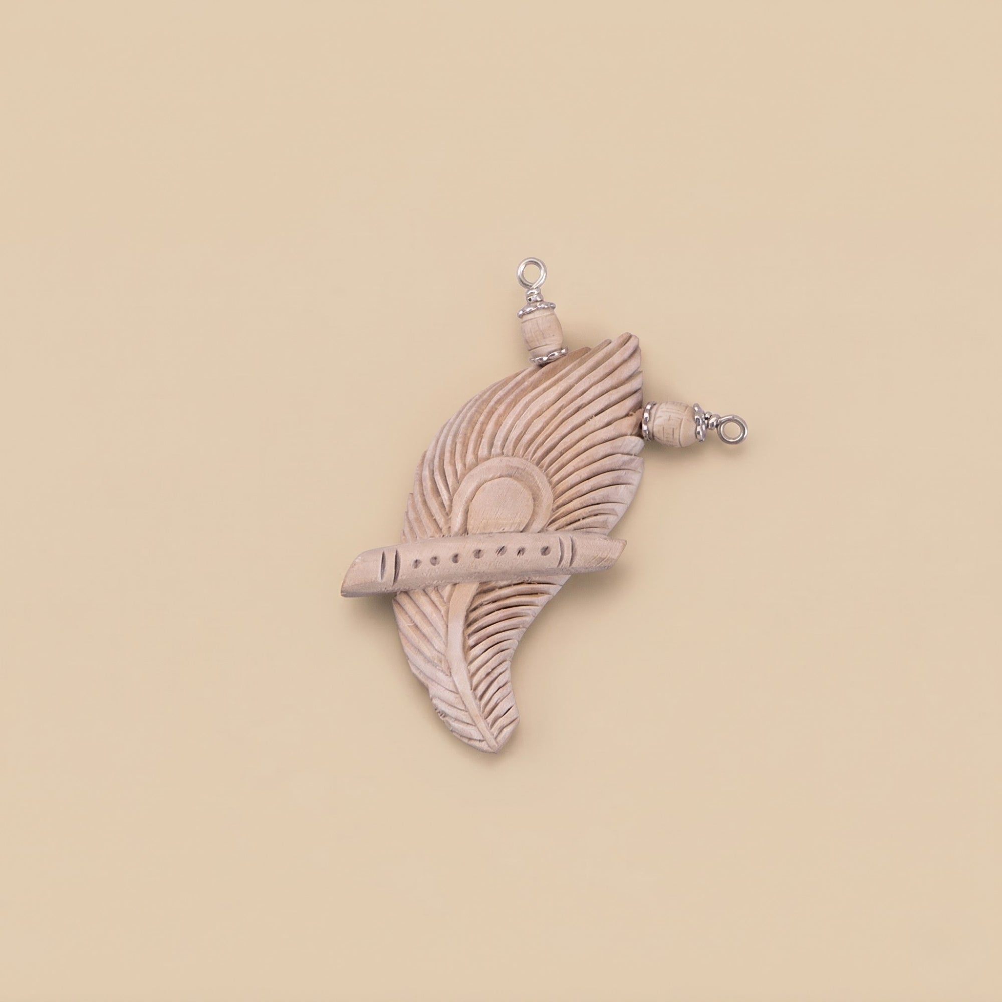 Close up flat lay of a silver pendant featuring authentic Tulsi wood carved into a flute and peacock feather