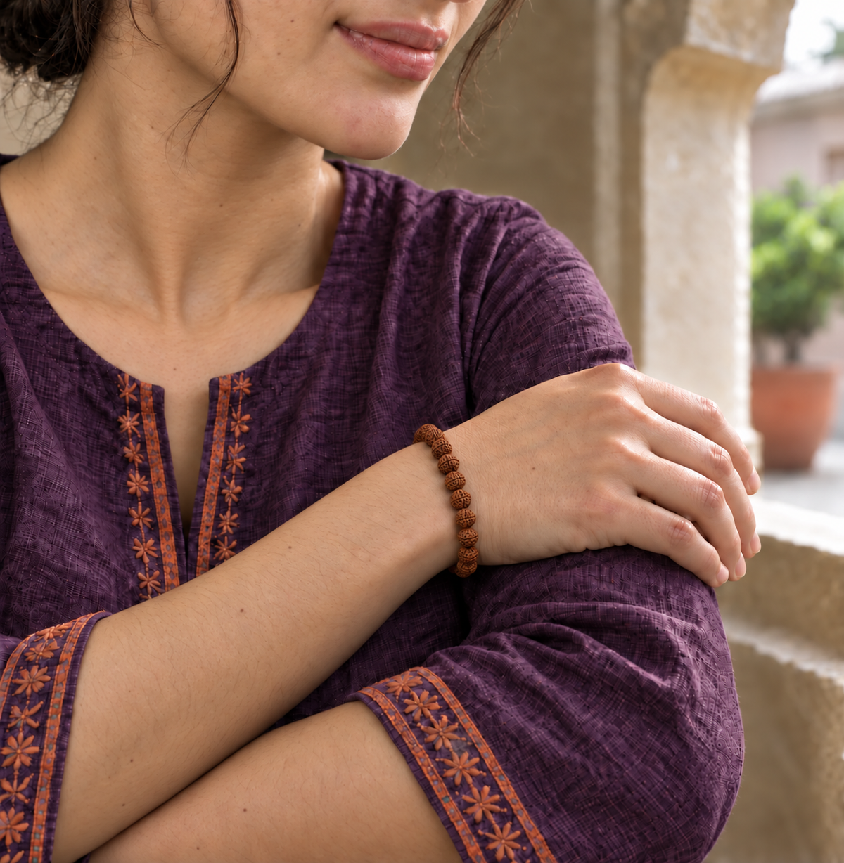 Small brown Rudraksha bead bracelet worn on a woman's wrist with a purple embroidered kurta.