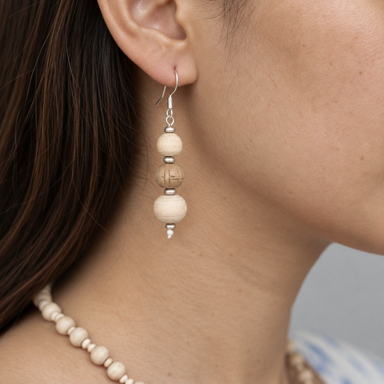 Tulsi drop earring with three round wooden beads, a carved centre bead and silver-toned spacers worn on the ear.