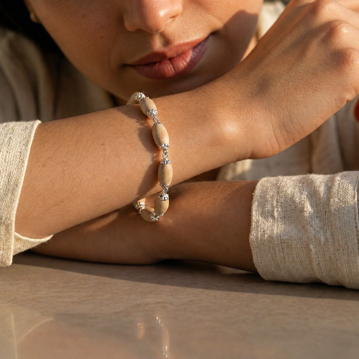 Tulsi bracelet with oval wooden beads, decorative silver-toned caps and connecting links worn on a woman's wrist.