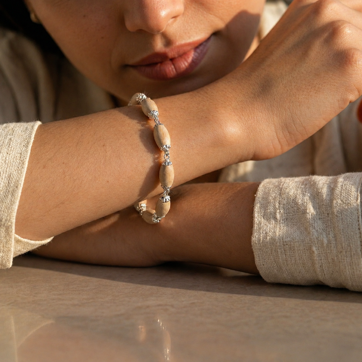 Tulsi bracelet with oval wooden beads, decorative silver-toned caps and connecting links worn on a woman's wrist.