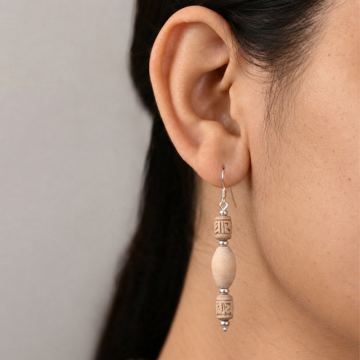 Tulsi drop earring with an oval centre bead, two carved barrel beads and silver-toned spacers worn on the ear.