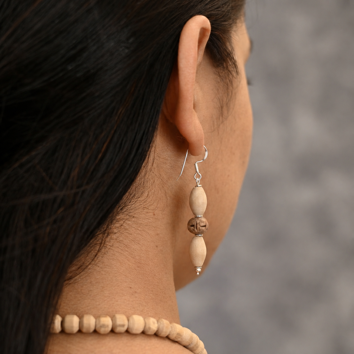 Tulsi drop earring with two oval wooden beads and a carved round centre bead, viewed from behind the ear.