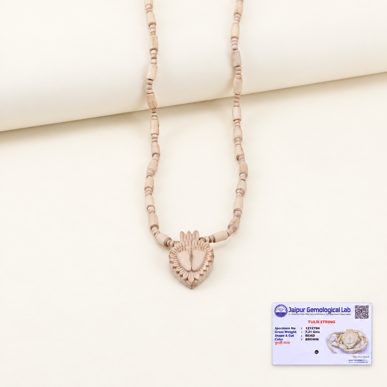 Tulsi bead mala with a carved heart pendant on an off-white background, with a certificate at the bottom right.