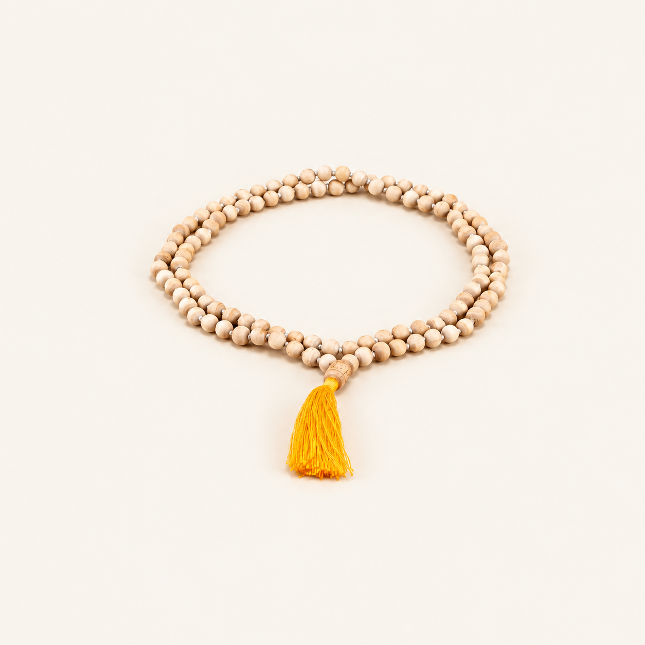 Tulsi japa mala with round wooden beads and a yellow tassel arranged on an off-white background.