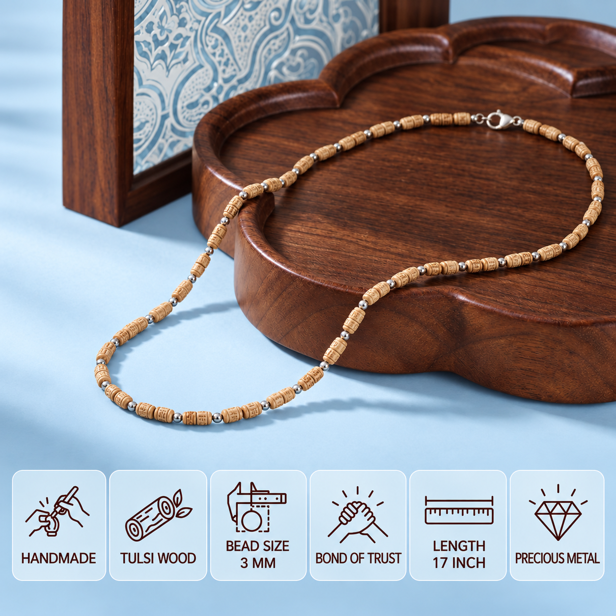 Tulsi mala with carved wooden beads and silver-tone spacers draped over a wooden tray on a pastel blue background, with product feature cards below.