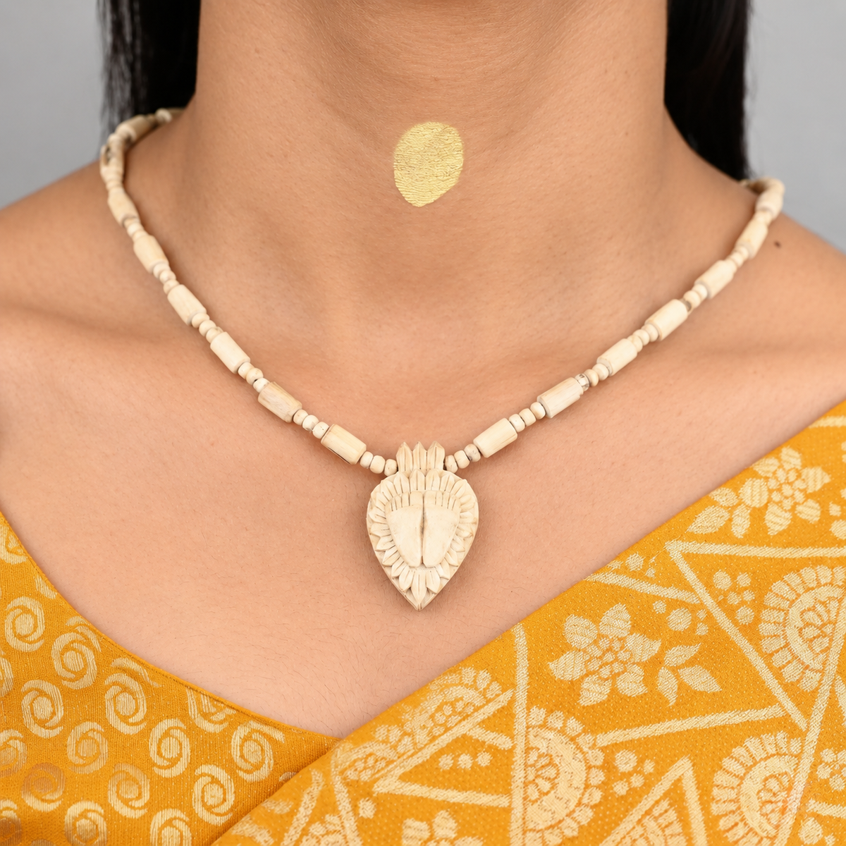 Tulsi mala with cylindrical beads and a carved lotus pendant featuring a pair of feet, worn with a yellow saree.