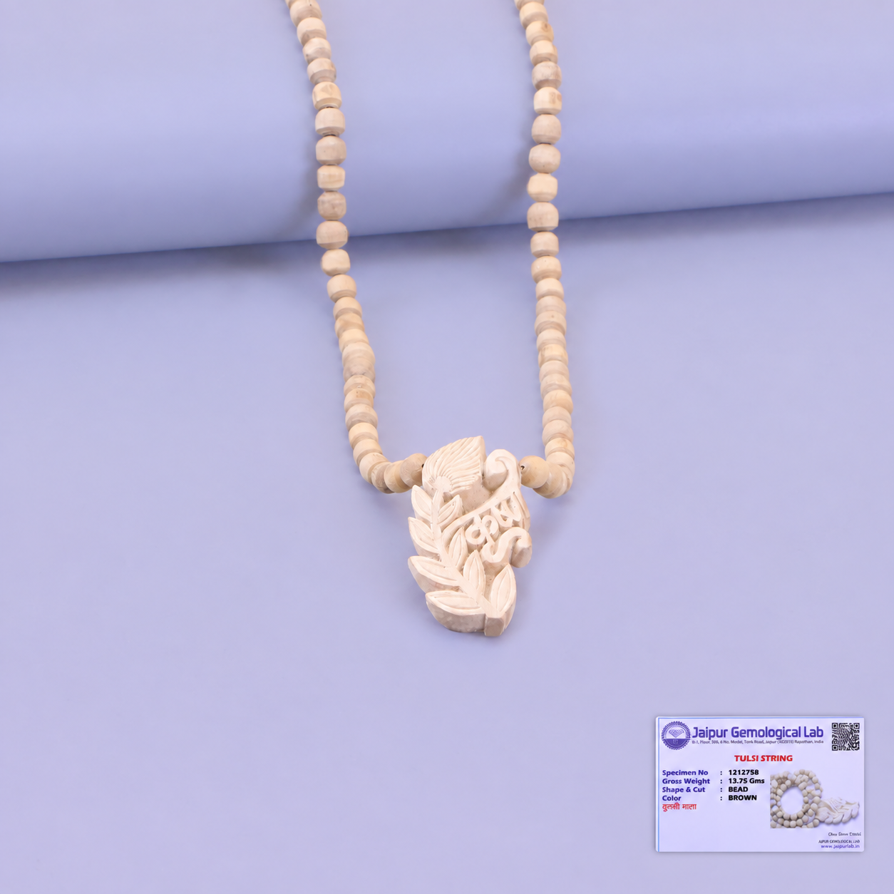 Tulsi bead mala with a carved leaf pendant displayed against a lilac background.