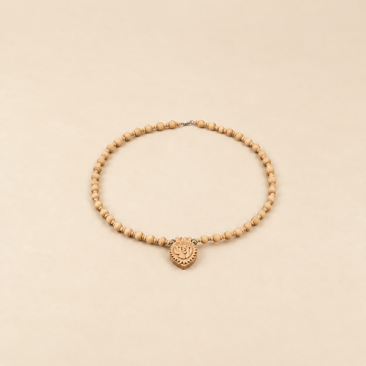 Tulsi mala with light wooden beads, small spacers and a carved wooden pendant, arranged in an oval on a beige background.