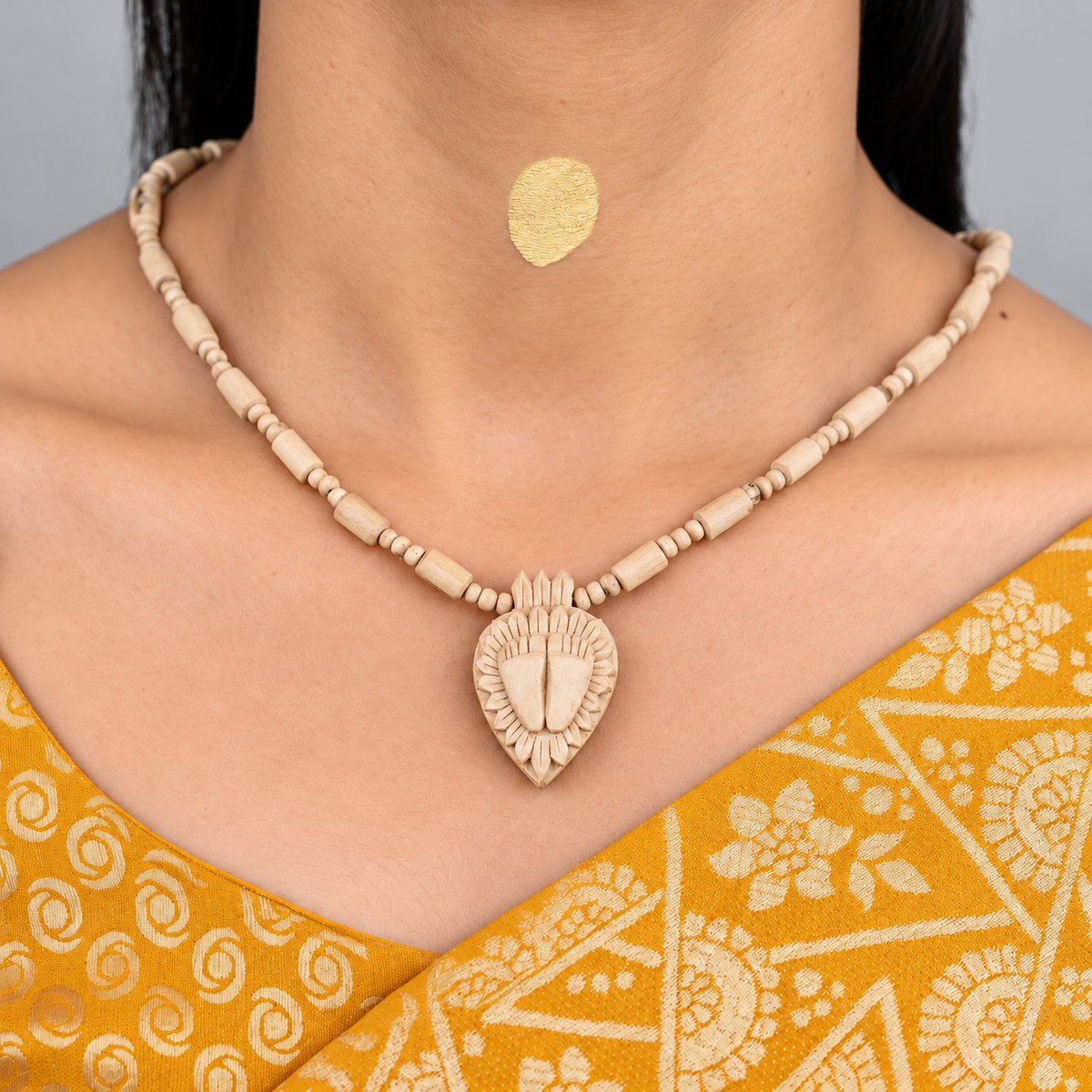 Woman wearing a Tulsi bead mala with a carved Charan Paduka pendant and a mustard saree.