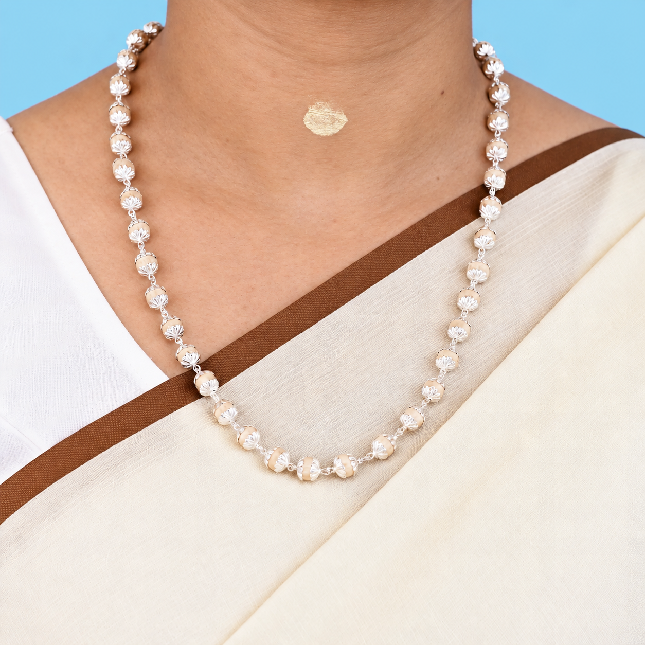 Tulsi mala with round wooden beads, floral silver-toned caps and chain links worn with a cream saree.