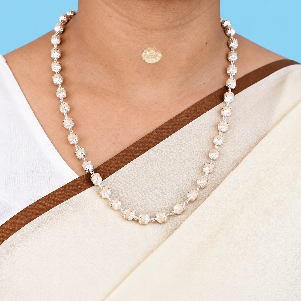 Tulsi mala with round wooden beads, floral silver-toned caps and chain links worn with a cream saree.