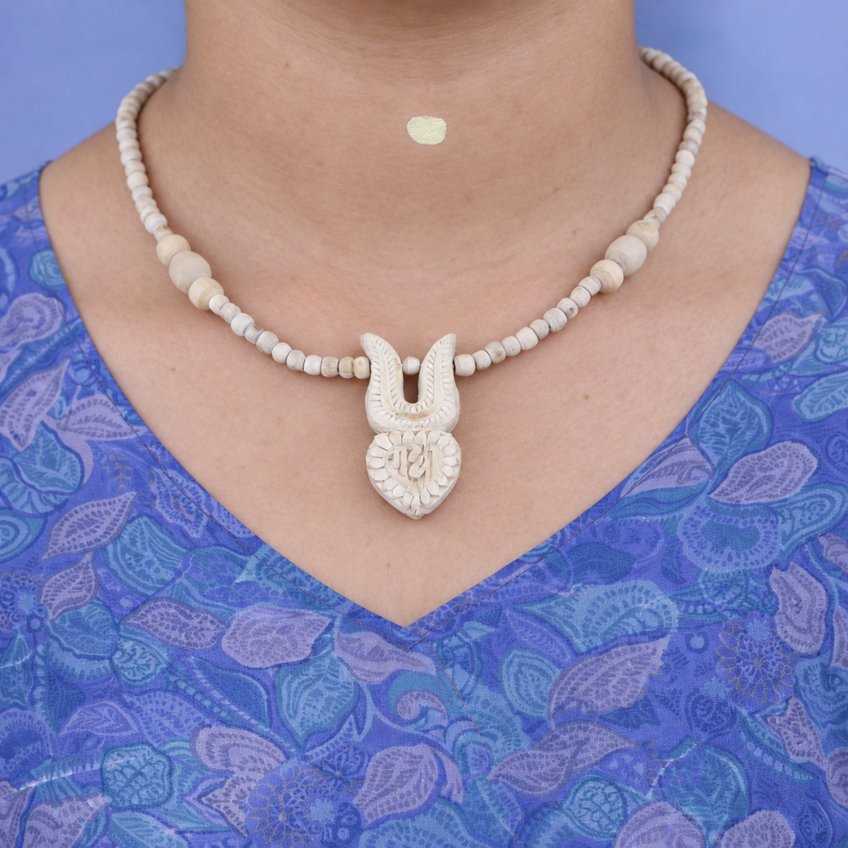 Tulsi bead mala with a carved tilak and heart-shaped Radha pendant worn with a blue printed kurta.